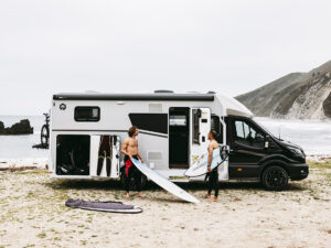 Halfintegraalcamper Sunlight UNLTD 2027 op het strand met twee surfers