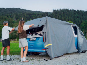 Twee personen bevestigen de Fiamma Cover Premium Van over een kampeerbus.
