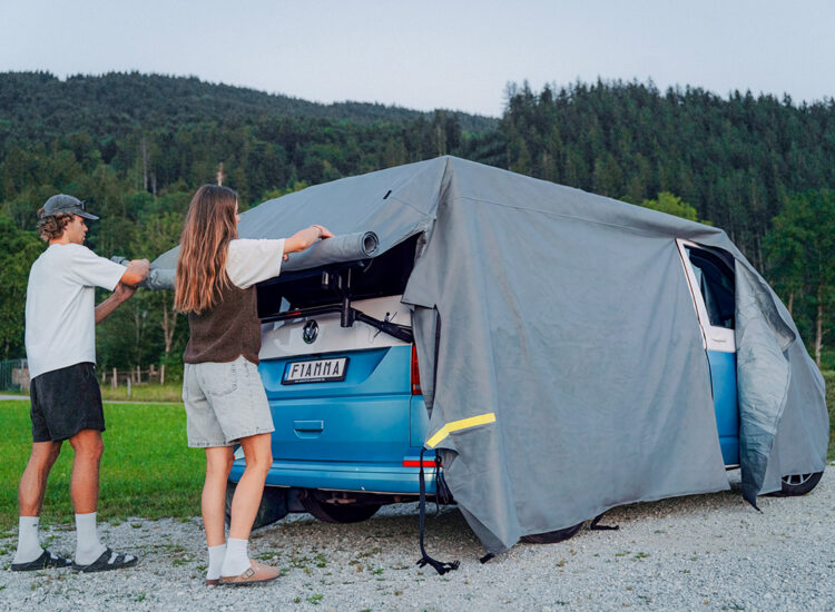Twee personen bevestigen de Fiamma Cover Premium Van over een kampeerbus.