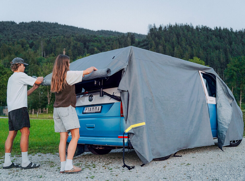 Twee personen bevestigen de Fiamma Cover Premium Van over een kampeerbus.