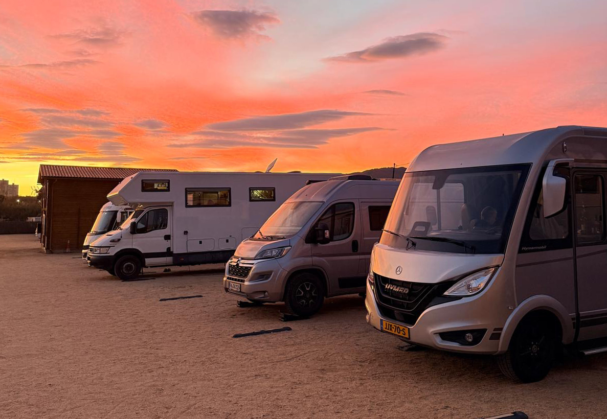 Campers op een camperplaats bij ondergaande zon onder een roze lucht.