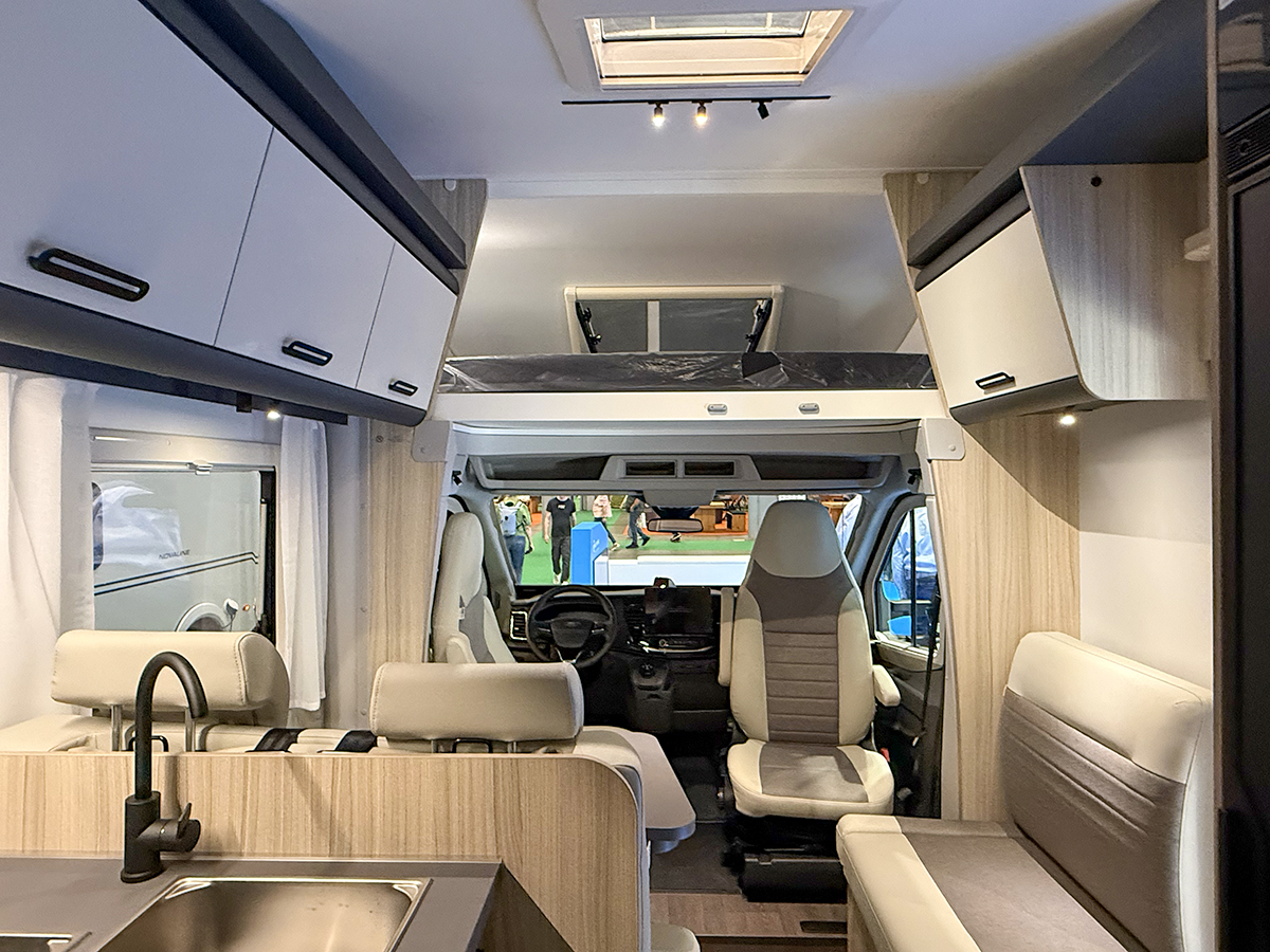 Doorkijkje in de alkoofcamper Sun Living A75 SL 20E met voorin de zitgroep en boven de cabine de alkoof met een tweepersoonsbed van 2,10 meter lang.